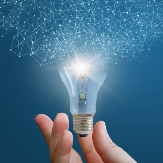 A hand holds a glowing light bulb against a blue background, with a network of glowing connections above, symbolizing innovation and ideas.