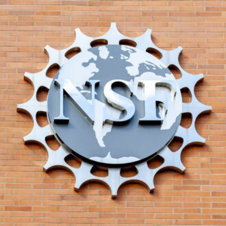 A metal National Science Foundation (NSF) logo is mounted on a brick wall, featuring a world map and gear-like border design.